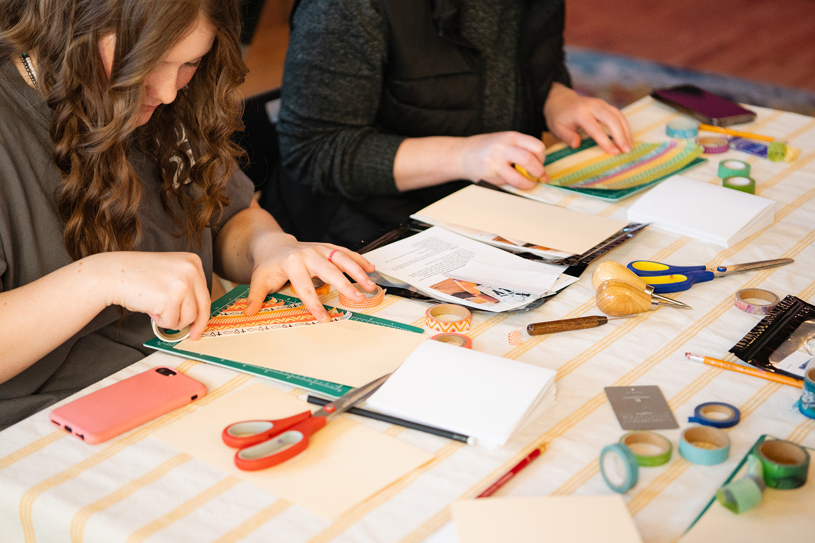 Person putting Washi tape on a book cover. Art and craft making supplies on a table