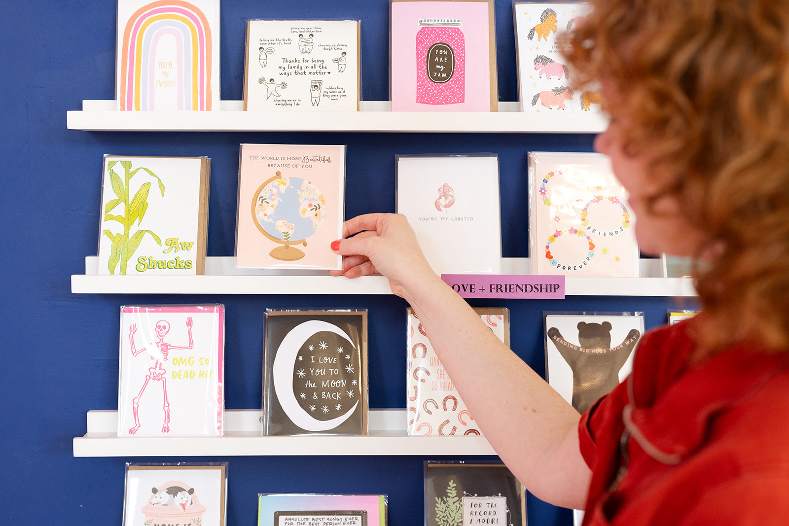 Person standing in front of a greeting card wall and holding a greeting card
