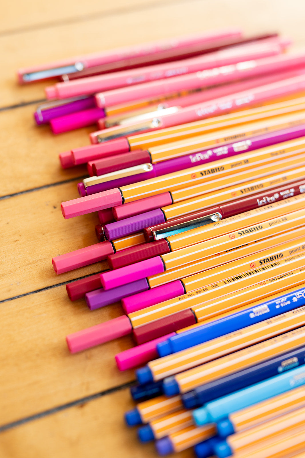 Many blue and pink pens on a wood floor