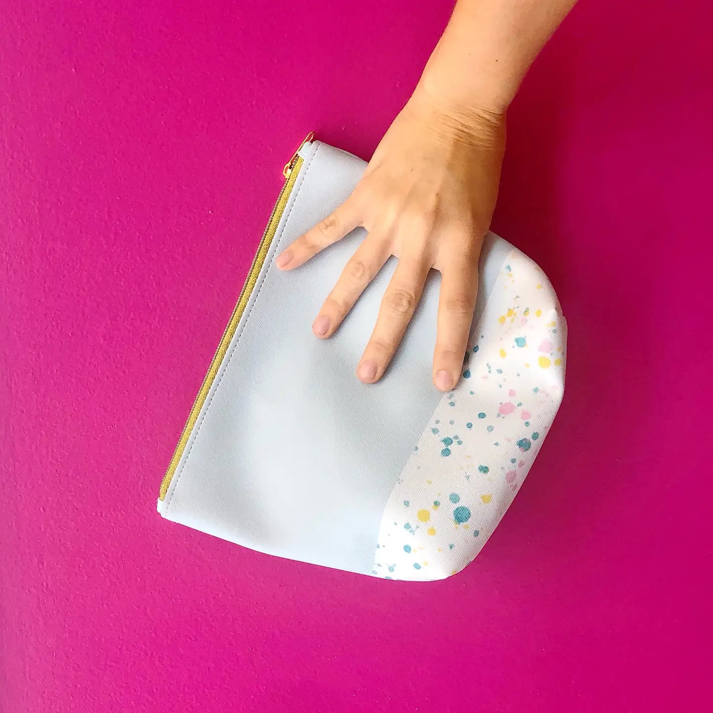 Hand holding a zip pouch against a pink background