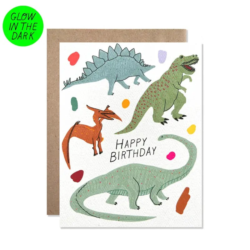 White greeting card with glow in the dark dinosaur illustrations. Black text “happy birthday”