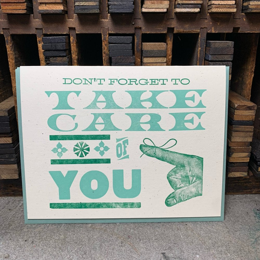 Cream-colored card. "Don't forget to take care of you" in green text. Green letter pressed picture of a pointing finger with string tied around the finger.
