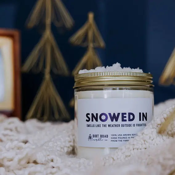 Candle jar with ‘Snowed In' label with decorative winter elements in the background