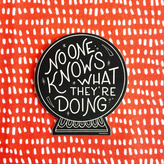 Black sticker on orange and white dotted background. Sticker is shaped like a crystal ball. White text on sticker reads "no one knows what they're doing"