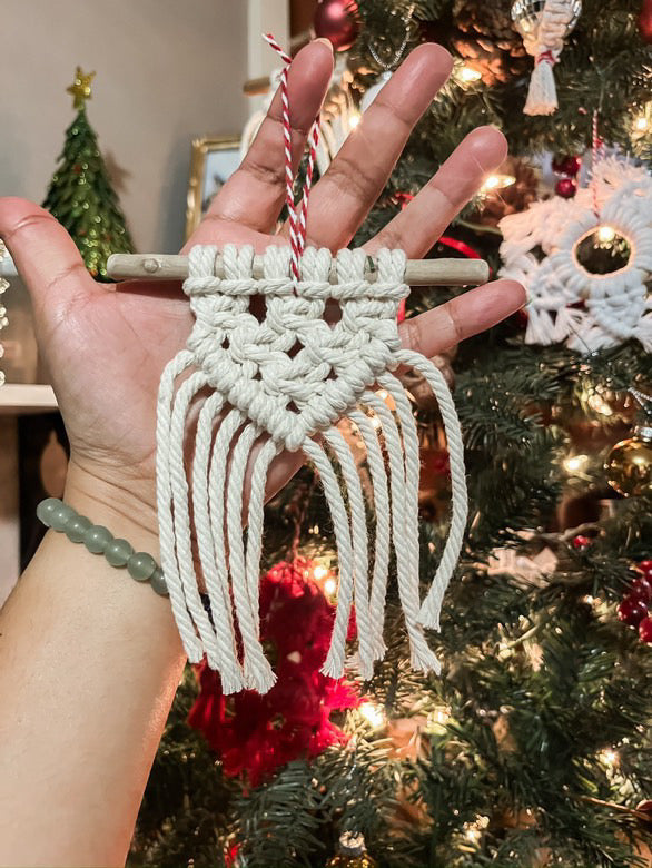 Hand holding macrame ornament in front of a holiday tree 