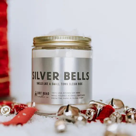 Clear jar filled with white candle. Silver label with dark silver text “silver bells” 