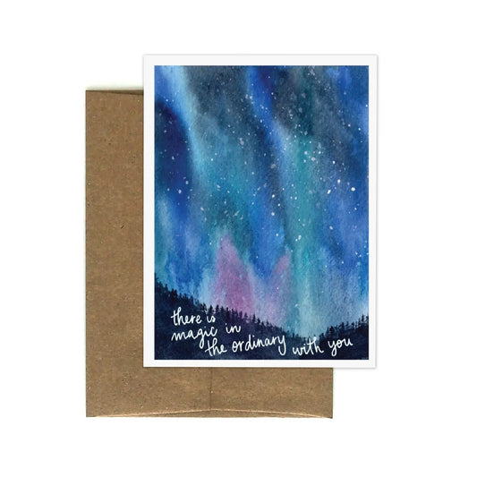 White greeting card with watercolor painting of the northern lights. White text on a black background “there is magic in the ordinary with you” 