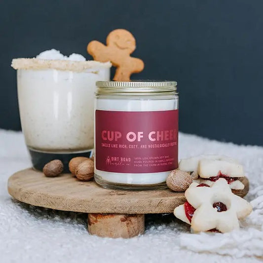 Clear jar filled with white candle. Cranberry colored label with metallic cranberry text “cup of cheer”