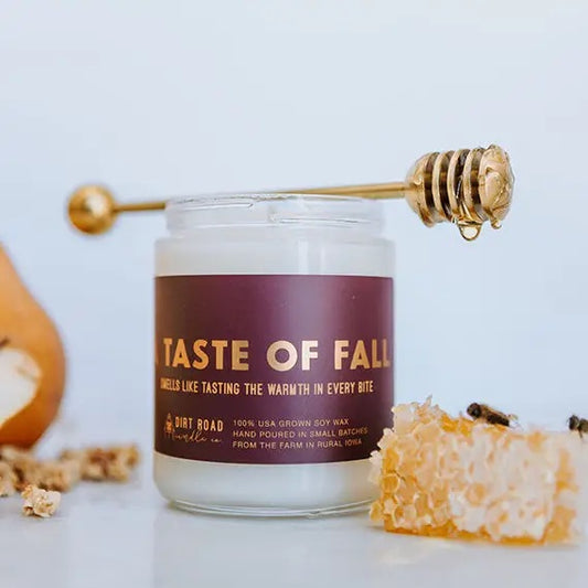 Clear jar with white candle and brown label. Gold lettering text reads "taste of fall." Honeycomb and honey decorations in the background of the photo. 