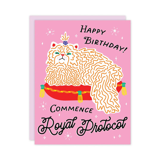 White card with full color pink background. Illustration of a fancy cat on a fancy pillow. Black text “happy birthday! Commence royal protocol” 