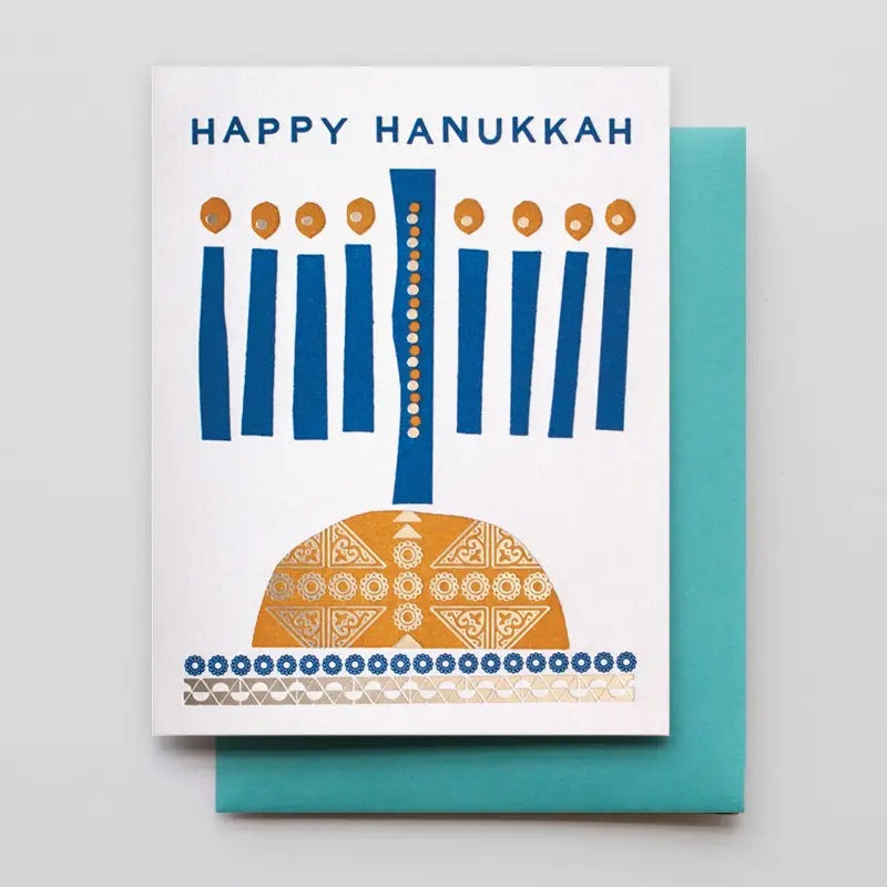 White card with abstract blue and gold menorah design. Blue text “happy Hanukkah”