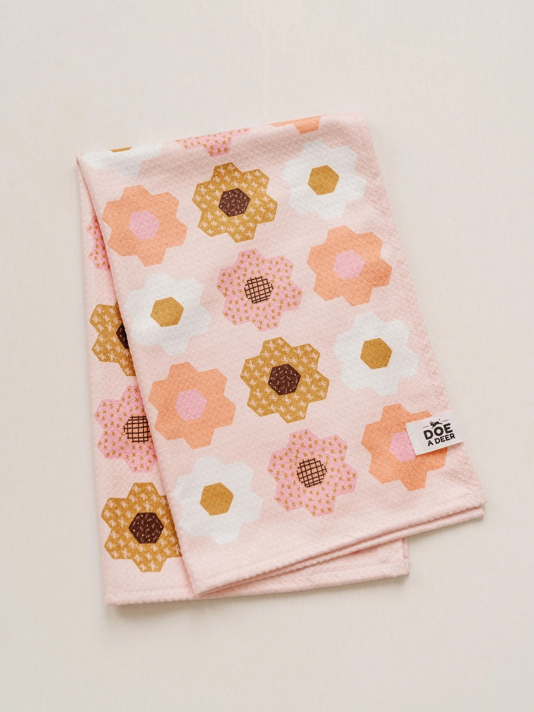 Front of kitchen towel. Light pink background with pink, orange, white, and mustard flower design 