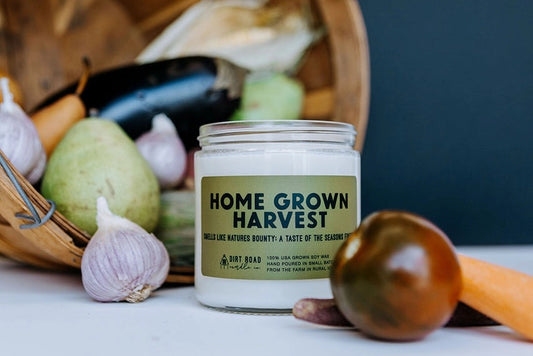 Clear jar filled with white candle. Green label. Dark green text on the label reads "Home Grown Harvest." Vegetables in a basket in the foreground as decoration. 