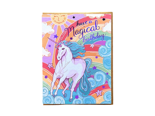 White card with full color rainbow background. Illustration of a unicorn. Purple foil text reads "have a magical birthday" 