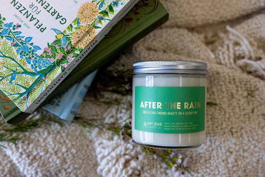 Clear jar filled with white candle. Green label with text “after the rain”