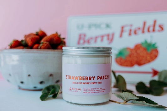 Clear jar filled with white candle. Pink label with text “strawberry patch”