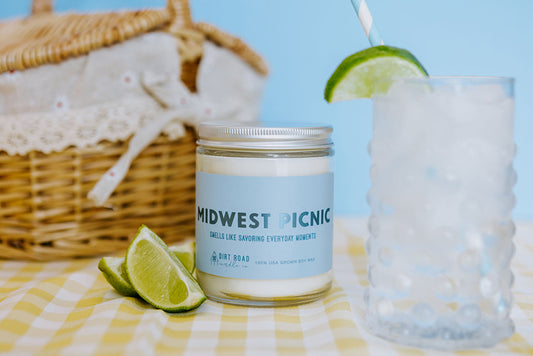 Clear jar filled with white candle. Blue label with text “Midwest picnic”