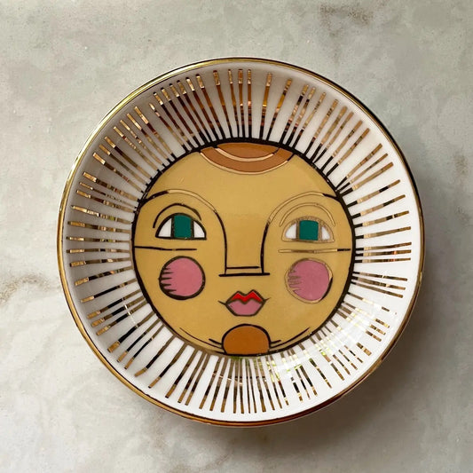 Small white plate with yellow, orange, pink sun face painted inside. Metallic gold lines. 