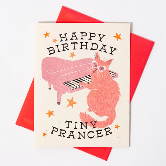 Cream card with illustration of a cat playing the piano. Black text "happy birthday tiny prancer" 