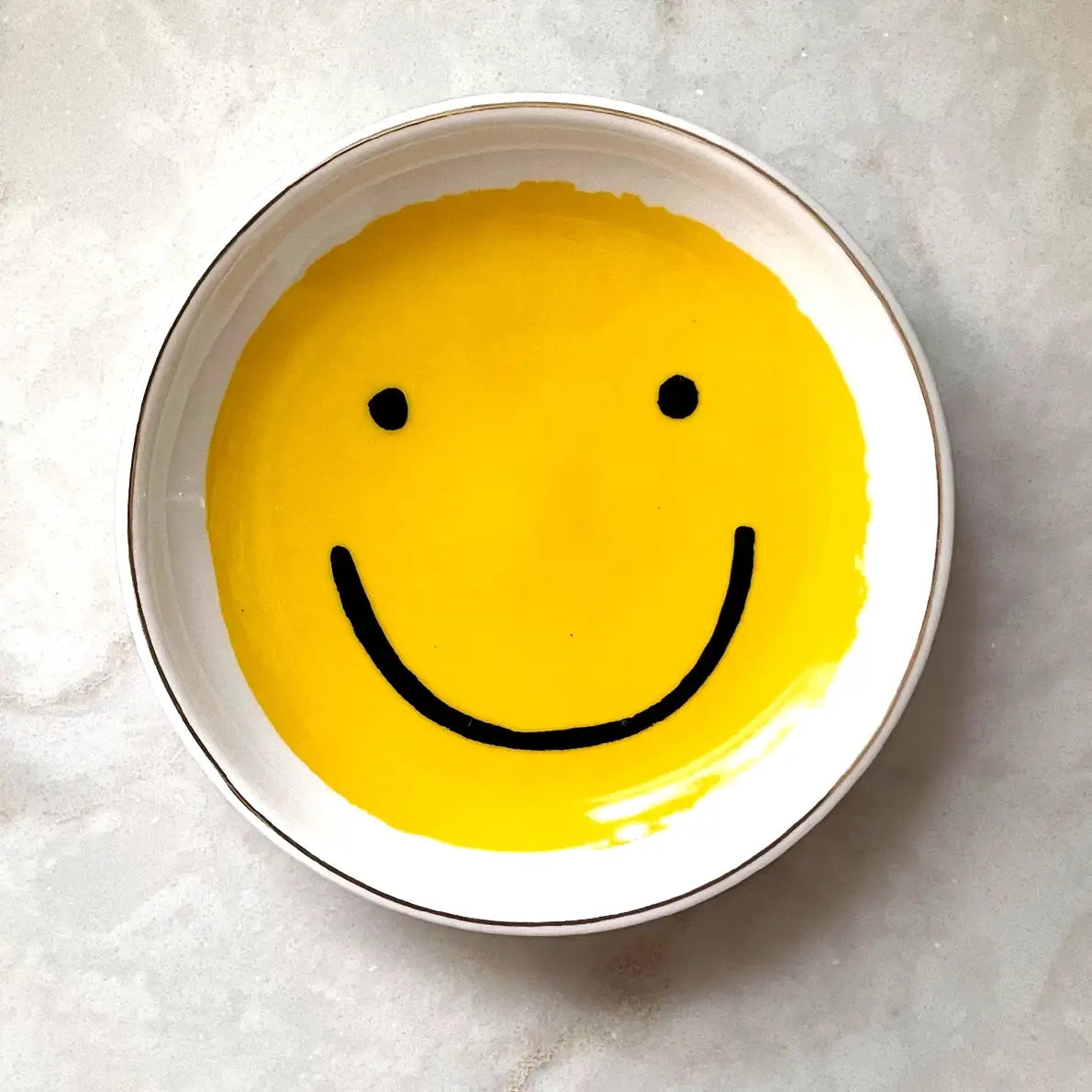 Circular white plate with yellow smiley face painted inside. 