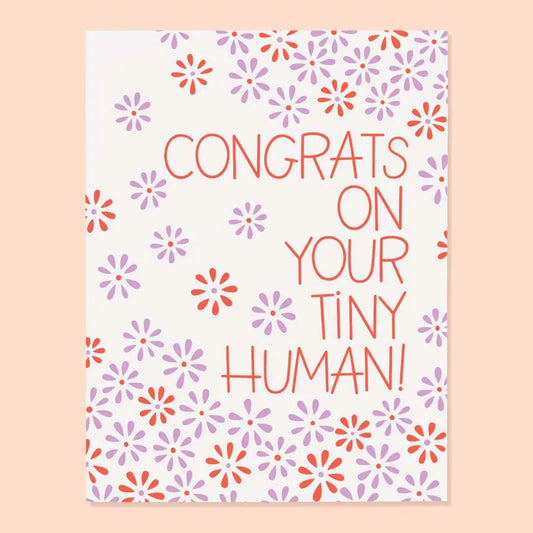 White greeting card with purple and red flower illustrations. Red text “congrats on your tiny human!”