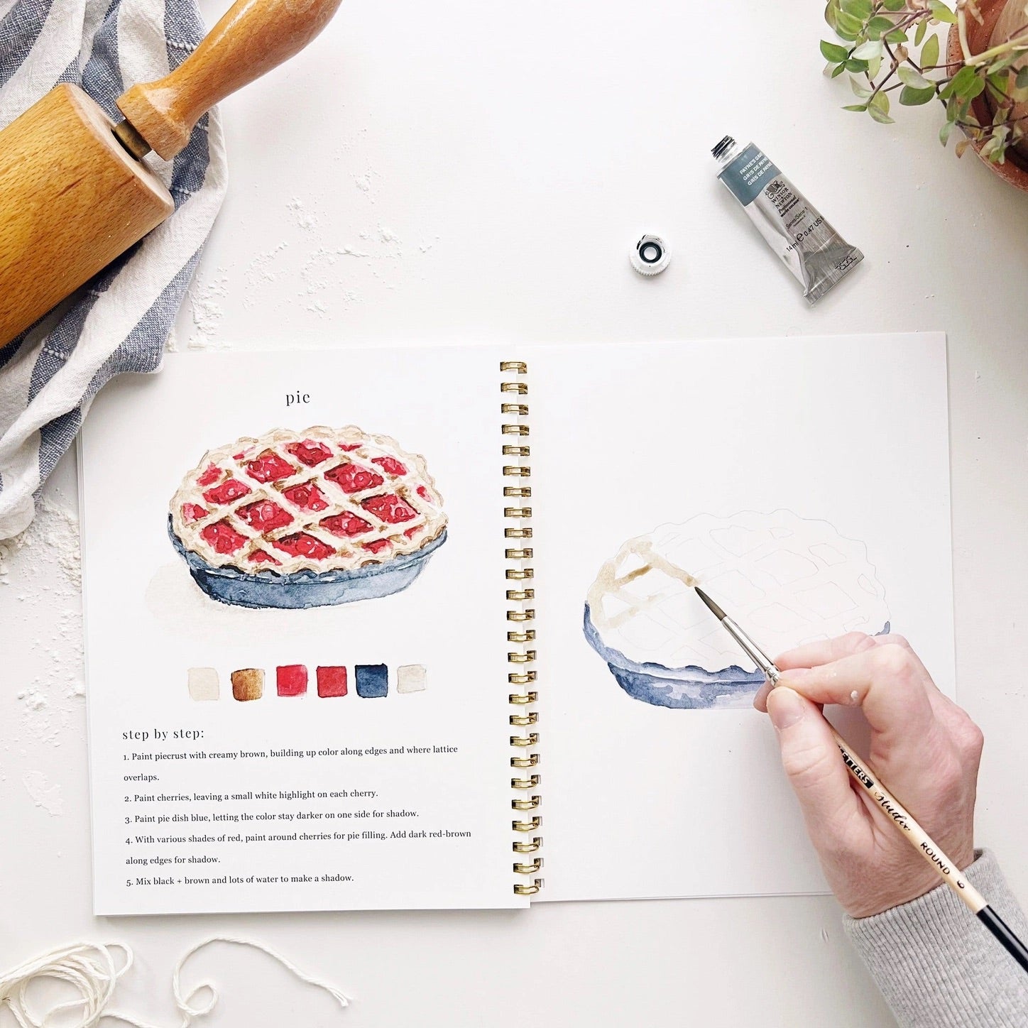 Inside view of watercolor workbook showing painting of a cherry pie 