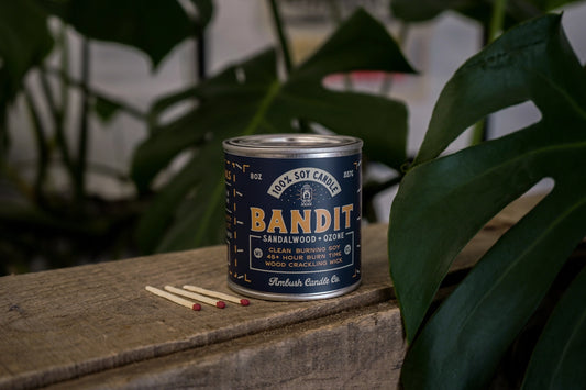 Candle in tin vessel. Dark red label with yellow text: bandit. 