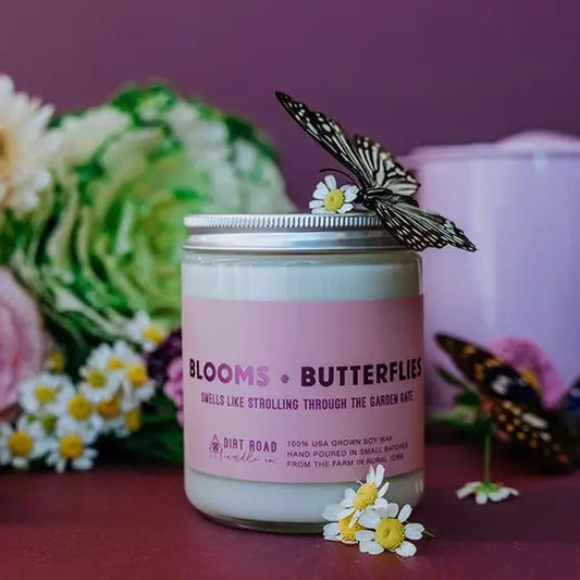 Candle with 'Blooms & Butterflies' label surrounded by flowers and butterflies on a pink background