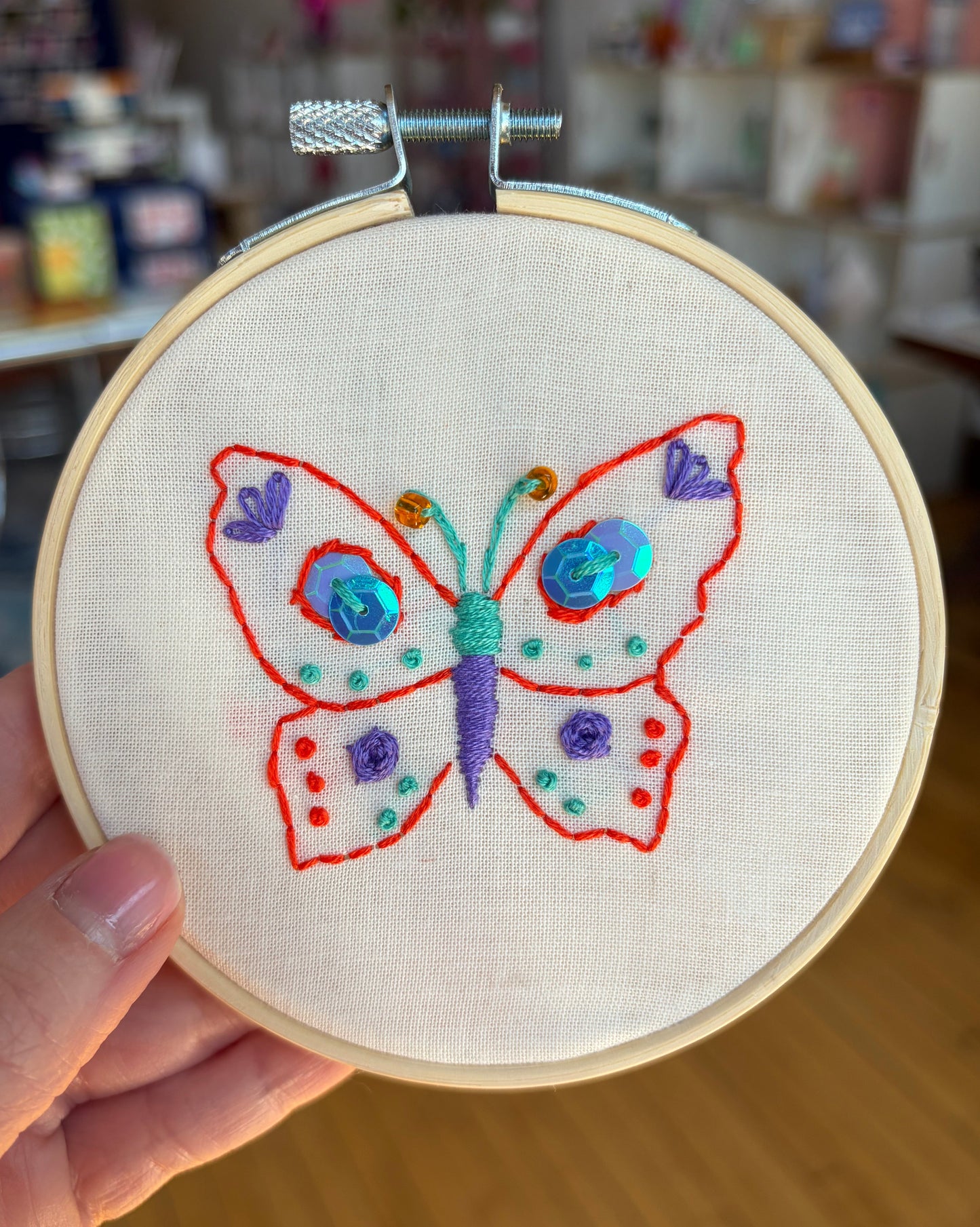 Embroidery hoop with a colorful butterfly design held by a hand.