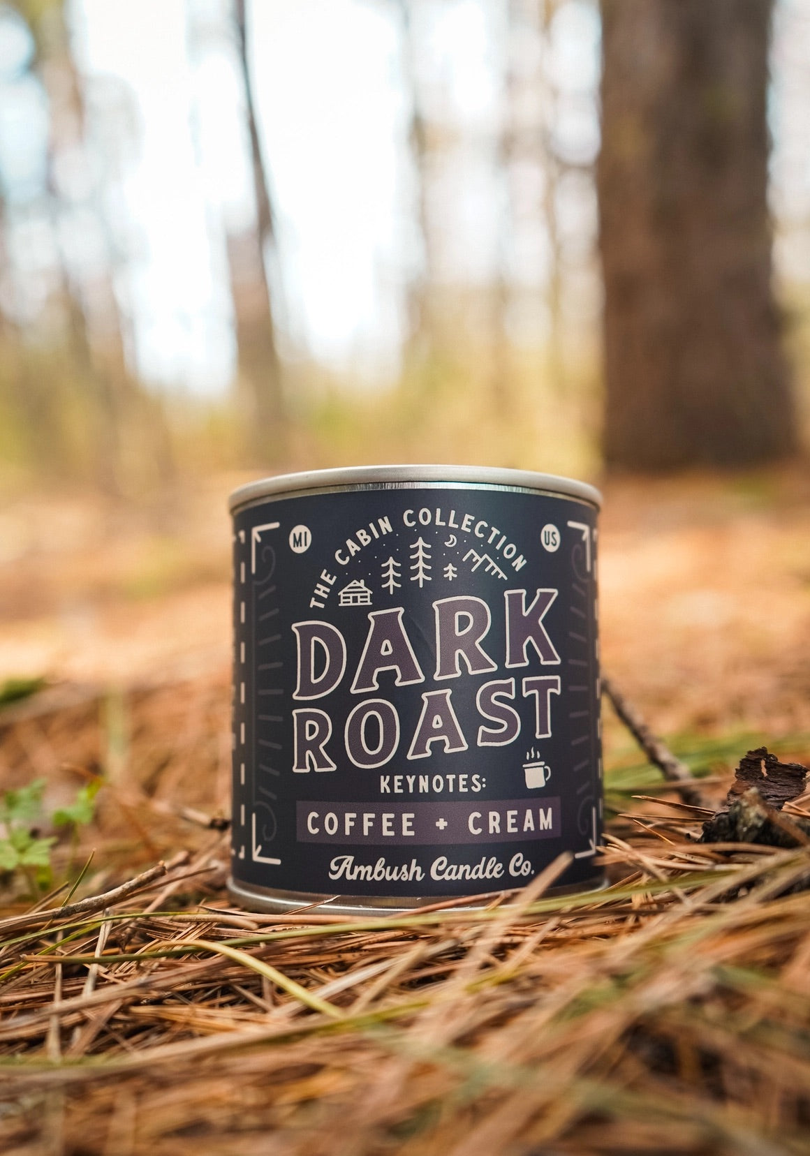 Candle in a tin vessel with a black label. Brown text on label reads "dark roast, coffee and cream" 