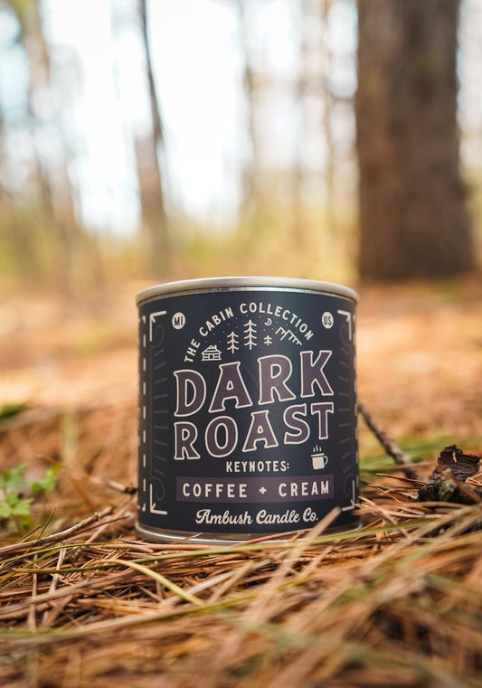 Candle in a tin vessel with a black label. Brown text on label reads "dark roast, coffee and cream" 