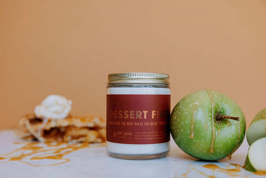 Candle jar with label “dessert first” on a table with apples 