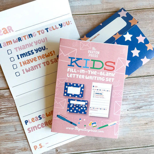Pink package titled 'Kids Fill-In-The-Blank Letter Writing Set' with stationery items on a wooden surface.