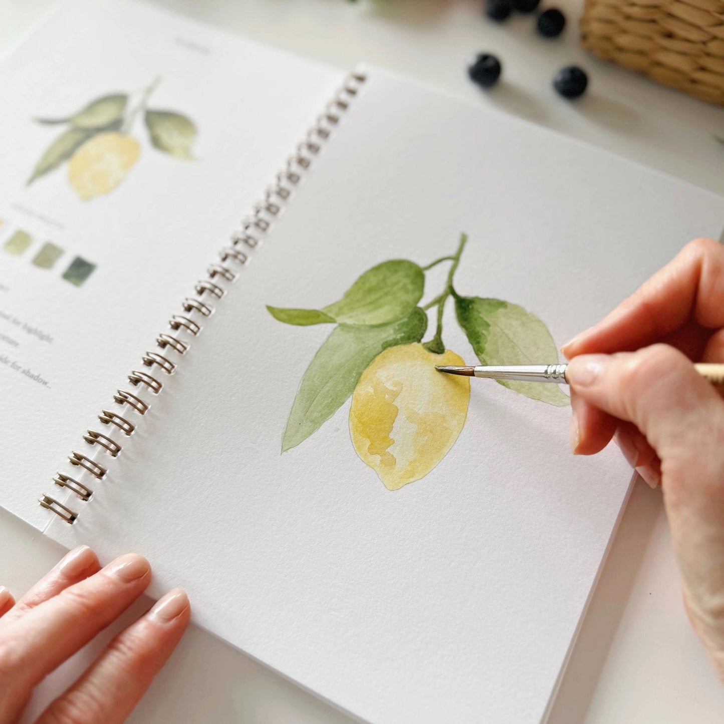 Person painting lemons on a notebook with a paintbrush