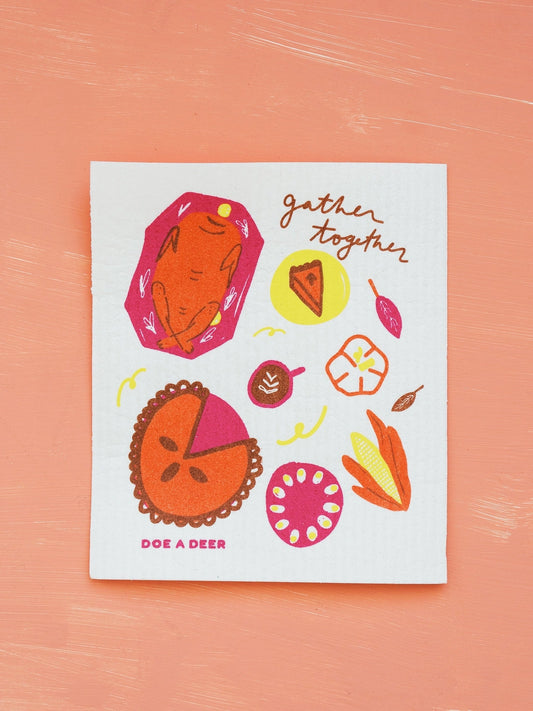 Swedish dish cloth with autumn-themed illustrations and 'gather together' text on a pink background