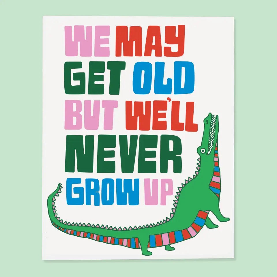 White card with alligator illustration. Multicolor text reads "we may get old but we'll never grow up." 