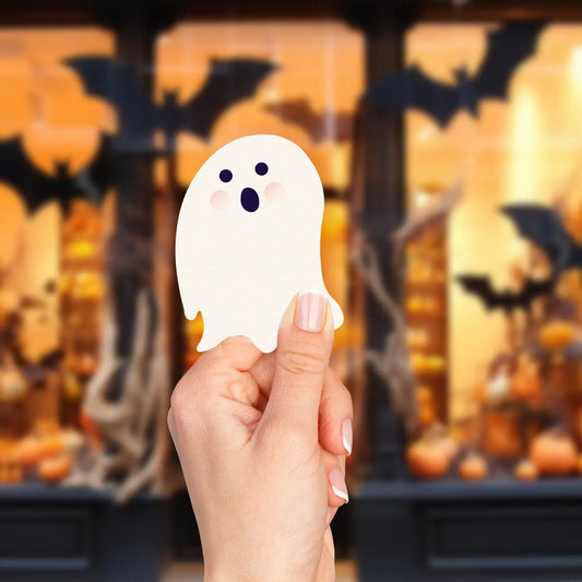 Hand holding a white ghost-shaped note with a Halloween-themed background