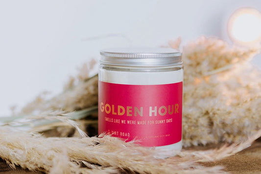 White candle in clear jar. Pink label with gold text: golden hour 