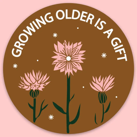 A round sticker with an illustration of three pink flowers and white text 'Growing Older is a Gift' on a brown background.