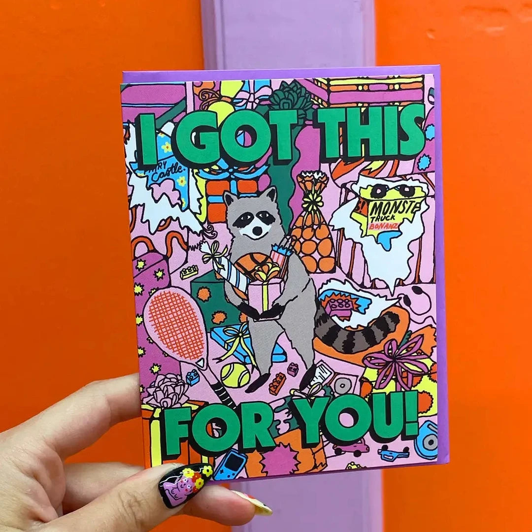 Colorful card with 'I Got This For You!' text  and raccoon illustration held against an orange background