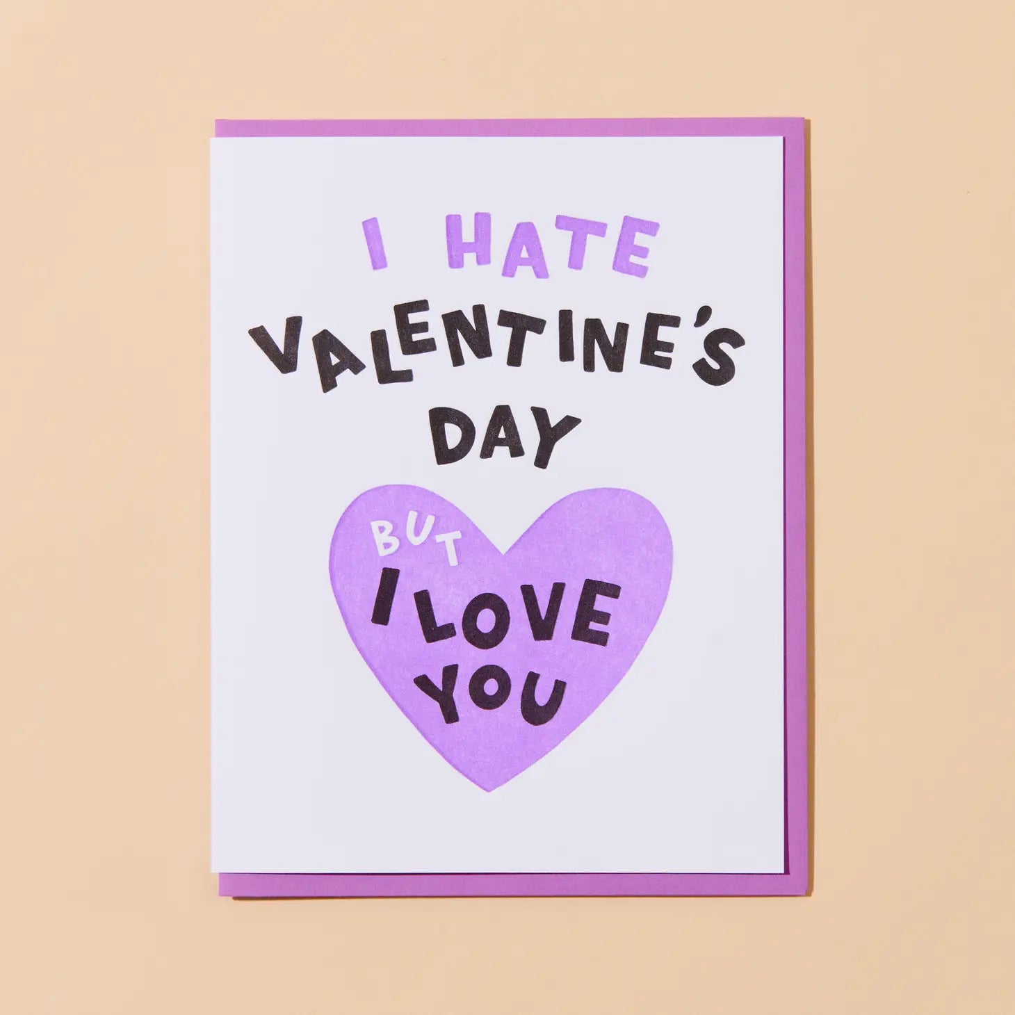 White card with purple heart. Purple, white, and black text reads "I hate Valentine's Day but I love you" 