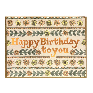 White card with cream background. Lines of yellow and orange flowers and green leaves. Shiny gold text reads "happy birthday to you"