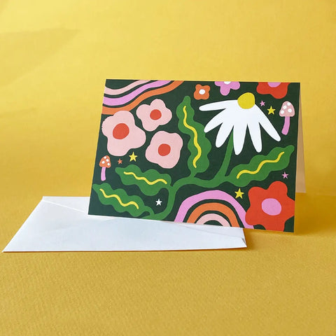 White card with dark green background and pink, white, and red flowers, green leaves, and pink and red rainbows. 
