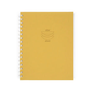 Front cover of spiral-bound notebook. Yellow background with dark yellow text that reads "slow down." 