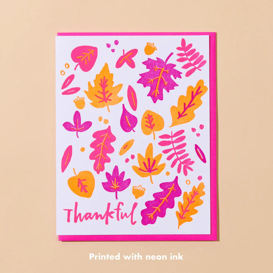 White card with neon pink and orange leaves. Pink text “thankful” 