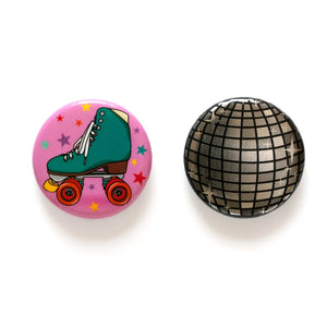 Set of two round magnets. One has a pink background with a turquoise roller skater. The other is a silver disco ball