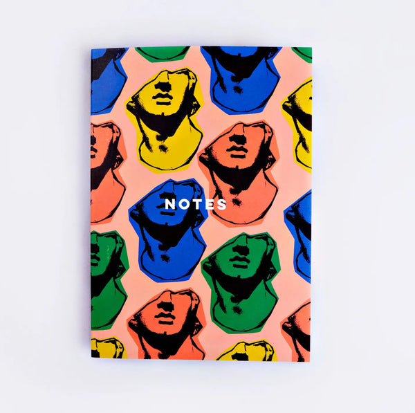 Front cover of a notebook with yellow, coral, blue, and green statue faces. White text reads "notes" 
