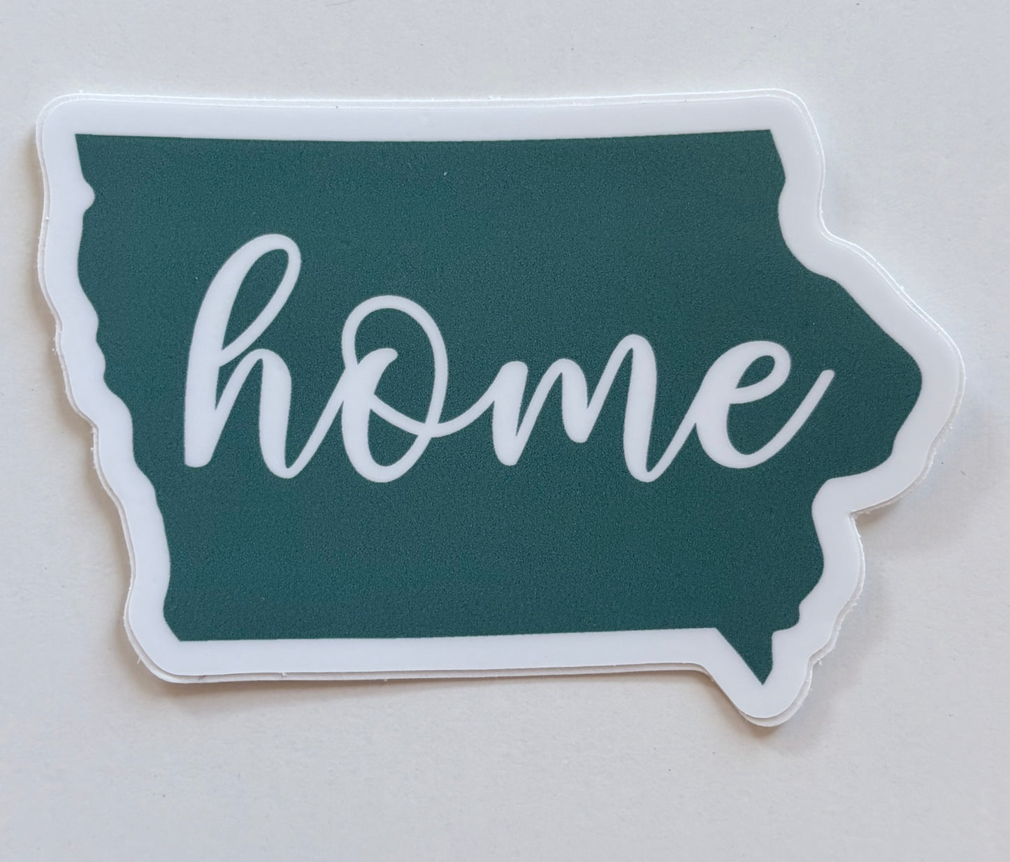 Sticker shaped like the state of Iowa with 'home' written on it, on a turquoise background