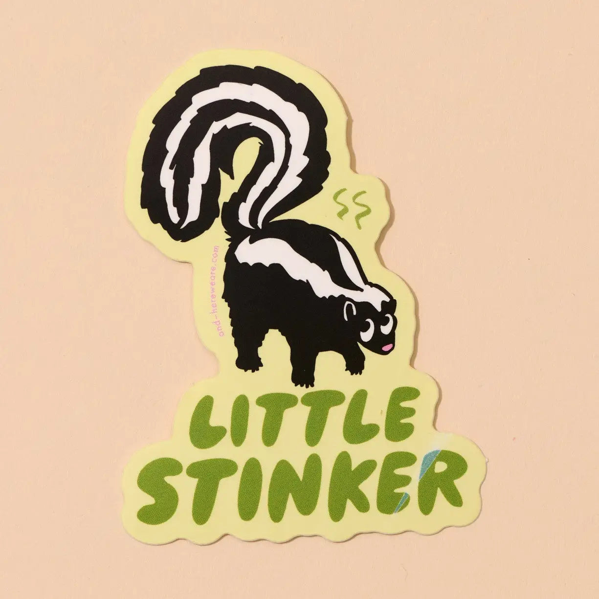 Sticker of a skunk with 'Little Stinker' green text on a beige background