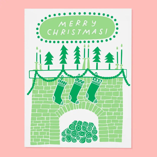 Greeting card with an illustration of a fireplace with stockings, trees, and 'Merry Christmas!' text on a pink background.